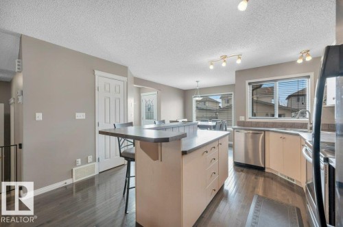 Kitchen featuring a central island with an extended breakfast bar, wood-finish flooring, stainless steel appliances, light-toned cabinetry, and a tile backsplash - 12063 19 Avenue, Edmonton, AB - Indoor Photo Showing Kitchen