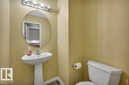 Powder room featuring a pedestal sink, round mirror, and a four-light vanity fixture - 12063 19 Avenue, Edmonton, AB - Indoor Photo Showing Bathroom