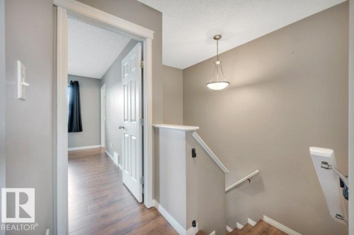 Interior hallway featuring wood-finish flooring, neutral wall tones, white trim, and a contemporary pendant light fixture - 12063 19 Avenue, Edmonton, AB - Indoor Photo Showing Other Room