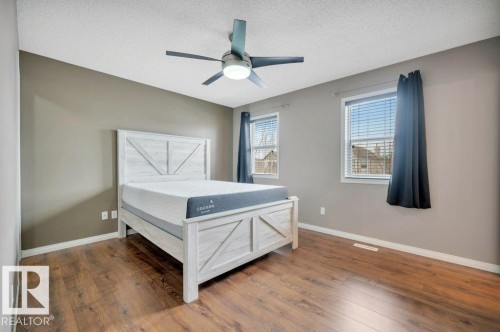 Bedroom featuring wood-finish flooring, two windows with blinds, a ceiling fan with integrated lighting, and neutral wall tones - 12063 19 Avenue, Edmonton, AB - Indoor Photo Showing Bedroom