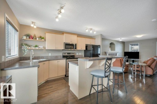 Open-concept kitchen featuring light-toned cabinetry, dark countertops, and stainless steel appliances - 12063 19 Avenue, Edmonton, AB - Indoor Photo Showing Kitchen