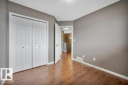 Room featuring wood-finish flooring, neutral gray walls, crisp white baseboards, and a paneled bifold closet door - 12063 19 Avenue, Edmonton, AB - Indoor Photo Showing Other Room