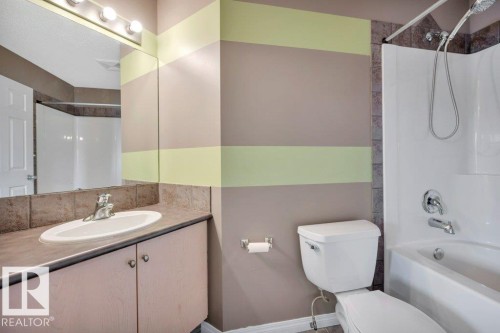 Full bathroom featuring a single vanity with an integrated sink, a wall-mounted mirror with overhead lighting, a toilet, and a shower-over-tub combination with a tiled surround - 12063 19 Avenue, Edmonton, AB - Indoor Photo Showing Bathroom