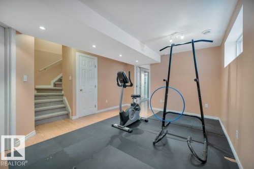 Finished basement featuring recessed lighting, wood-finish flooring, a white six-panel door, and a carpeted staircase with a white handrail - 12063 19 Avenue, Edmonton, AB - Indoor Photo Showing Gym Room