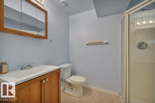 Bathroom featuring a wood-finish vanity with an integrated sink, a mirrored medicine cabinet, and a glass-enclosed shower - 12063 19 Avenue, Edmonton, AB - Indoor Photo Showing Bathroom