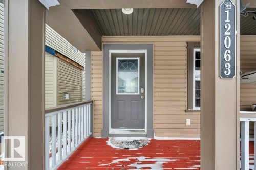 Covered front porch featuring a red-stained deck, white railing, and beige siding - 12063 19 Avenue, Edmonton, AB - Outdoor With Exterior