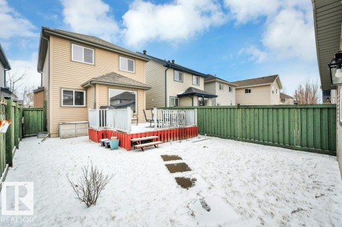 Rear exterior featuring a spacious wooden deck with white railings, tan vinyl siding, multiple windows, and a green privacy fence enclosing the yard - 12063 19 Avenue, Edmonton, AB - Outdoor With Deck Patio Veranda With Exterior