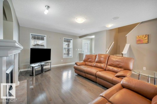 Open concept living area featuring wood-finish flooring, a white mantel fireplace with a tile surround, and multiple windows with blinds - 12063 19 Avenue, Edmonton, AB - Indoor Photo Showing Living Room