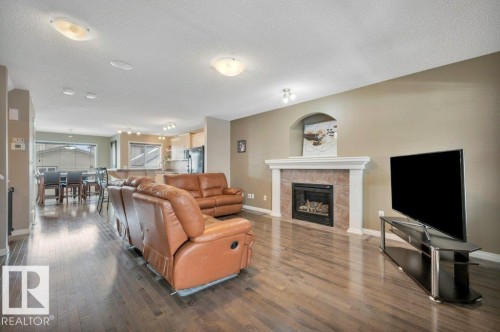 Spacious living area featuring wood-finish flooring, a fireplace with a tiled surround and white mantel, and ceiling-mounted lighting fixtures - 12063 19 Avenue, Edmonton, AB - Indoor Photo Showing Living Room With Fireplace