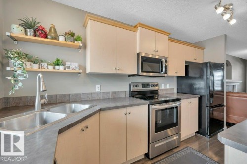 Kitchen featuring light-toned cabinetry with crown molding, stainless steel appliances, and a double basin sink - 12063 19 Avenue, Edmonton, AB - Indoor Photo Showing Kitchen With Double Sink