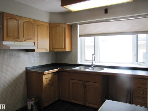 Kitchen featuring wood-finish cabinetry and dark countertops - 7135 87 Street, Edmonton, AB - Indoor Photo Showing Kitchen With Double Sink