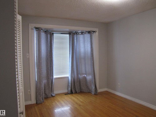 Bright room featuring a large window with blinds and drapes, light-toned walls, wood-finish flooring, and white trim - 7135 87 Street, Edmonton, AB - Indoor Photo Showing Other Room