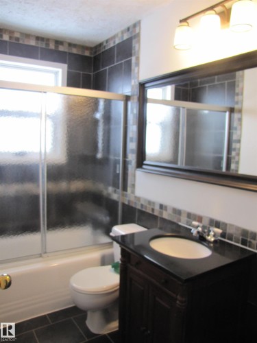 Bathroom featuring a dark wood-finish vanity with an integrated sink and black countertop - 7135 87 Street, Edmonton, AB - Indoor Photo Showing Bathroom
