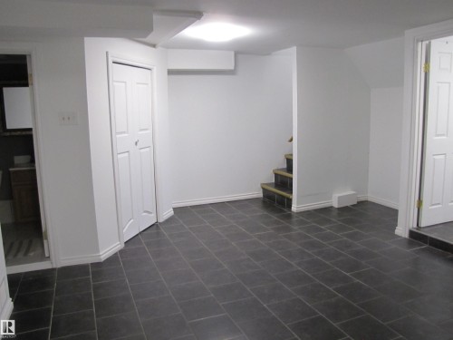 Spacious area featuring dark rectangular floor tiles, white baseboards, and a built-in closet with bifold doors - 7135 87 Street, Edmonton, AB - Indoor Photo Showing Other Room