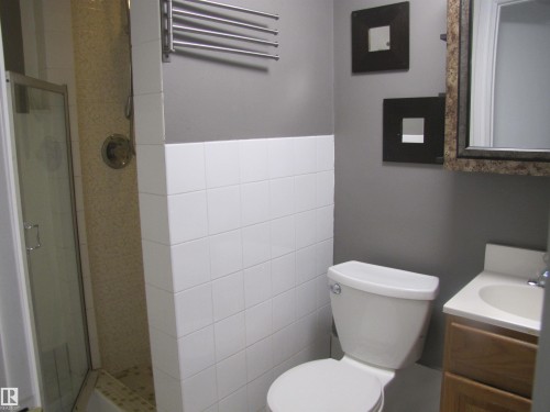 Bathroom featuring a glass-enclosed shower, white tile accents, a wall-mounted towel rack, a toilet, and a vanity with an integrated sink - 7135 87 Street, Edmonton, AB - Indoor Photo Showing Bathroom