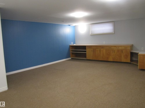 Spacious room featuring carpeting, a light blue accent wall, a built-in wood-finish cabinet system with integrated shelving, and recessed lighting - 7135 87 Street, Edmonton, AB - Indoor