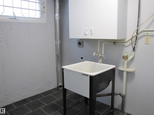 Utility sink featuring a white basin on a black-frame stand, wall-mounted white cabinetry, and dark-toned tile flooring - 7135 87 Street, Edmonton, AB - Indoor