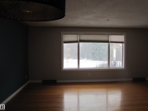 Spacious interior room featuring wood-finish flooring, a large multi-pane window, and a dark accent wall - 7135 87 Street, Edmonton, AB - Indoor Photo Showing Other Room
