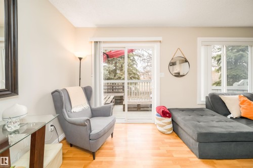 Living area featuring wood-finish flooring, light-toned walls, and a sliding glass door providing exterior access to a wood-decked outdoor space - 50 14603 Miller Boulevard, Edmonton, AB - Indoor Photo Showing Living Room