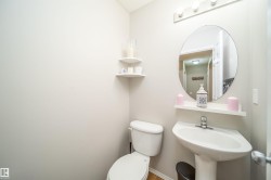 Powder room featuring a pedestal sink, round wall mirror, and white wall-mounted shelving - 