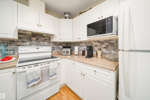 Kitchen featuring white cabinetry, a white electric range with a matching range hood, and an over-the-range microwave - 50 14603 Miller Boulevard, Edmonton, AB - Indoor Photo Showing Kitchen