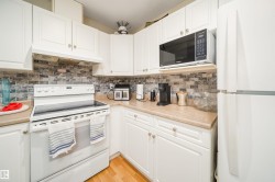 Kitchen featuring white cabinetry, a white electric range with a matching range hood, and an over-the-range microwave - 