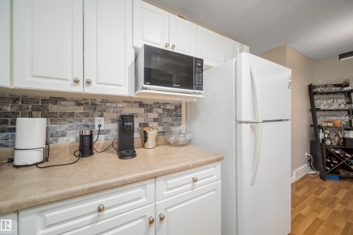 Kitchen featuring white cabinetry, light-toned countertops, and a mosaic tile backsplash - 50 14603 Miller Boulevard, Edmonton, AB - Indoor Photo Showing Kitchen