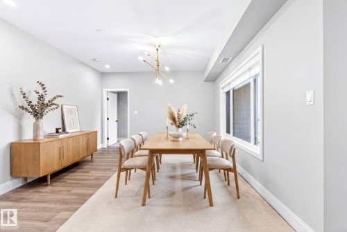 Dining area featuring wood-finish flooring, a contemporary linear chandelier, recessed lighting, and a large window with white trim - 520 7463 May Common, Edmonton, AB - Indoor Photo Showing Dining Room