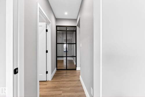 Modern hallway featuring a full-light black-framed glass door, light wood-finish flooring, recessed lighting, white baseboards, and matte black door hardware - 520 7463 May Common, Edmonton, AB - Indoor Photo Showing Other Room
