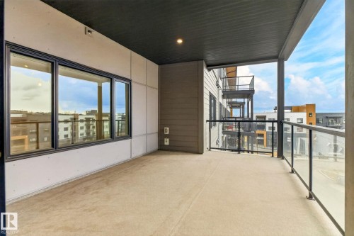 Spacious private balcony featuring a concrete floor, dark soffit ceiling with recessed lighting, and a modern glass and metal railing - 520 7463 May Common, Edmonton, AB - Outdoor With Exterior