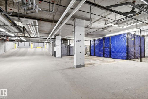 Underground parking garage featuring concrete flooring, exposed ceiling utilities, bright overhead lighting, and dedicated storage units - 520 7463 May Common, Edmonton, AB - Indoor