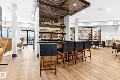 Bar area featuring a dark countertop, integrated shelving, and three upholstered bar stools - 520 7463 May Common, Edmonton, AB - Indoor