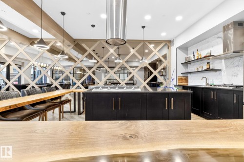 Gourmet kitchen featuring a large central island, dark cabinetry, and a stainless steel range hood - 520 7463 May Common, Edmonton, AB - Indoor