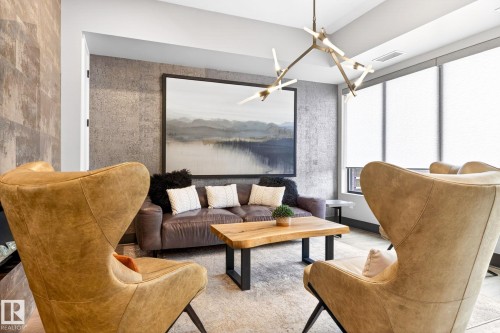 Living area featuring a modern linear chandelier, textured accent wall, and large windows with roller shades - 520 7463 May Common, Edmonton, AB - Indoor Photo Showing Living Room