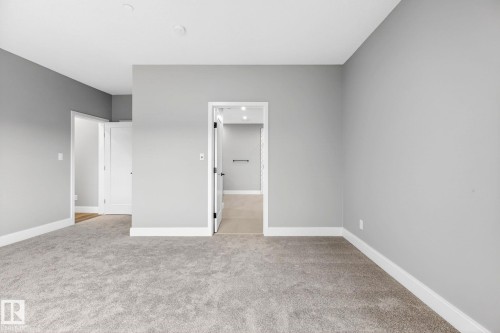 Spacious room featuring neutral gray walls, plush gray carpeting, and crisp white baseboards - 520 7463 May Common, Edmonton, AB - Indoor Photo Showing Other Room