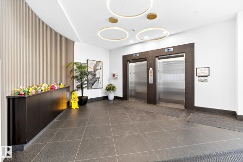 Lobby area featuring two stainless steel elevators, recessed accent lighting, a textured vertical panel wall, and large format floor tiling - 520 7463 May Common, Edmonton, AB - Indoor Photo Showing Other Room