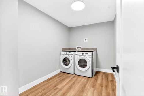 Laundry area featuring wood-finish flooring and a neutral color palette - 520 7463 May Common, Edmonton, AB - Indoor Photo Showing Laundry Room