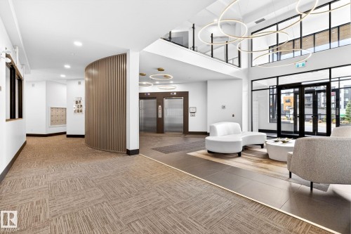 Spacious lobby featuring high ceilings, contemporary light fixtures, a multi-level layout, and large glass entry doors - 520 7463 May Common, Edmonton, AB - Indoor Photo Showing Other Room