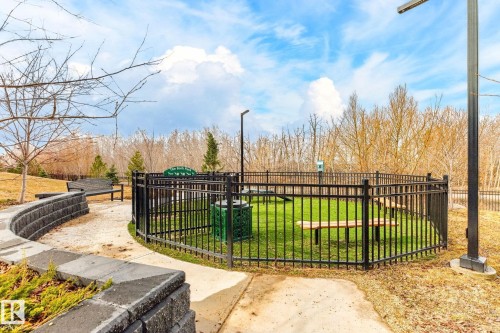Fenced outdoor area with green space, featuring a black metal fence, built-in benches, and a light post - 520 7463 May Common, Edmonton, AB - Outdoor