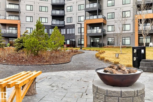 Common area featuring a stone paver patio, a bowl-style fire pit on a block base, and a gravel pathway - 520 7463 May Common, Edmonton, AB - Outdoor With Facade