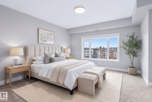 Bedroom featuring a large window, light gray walls, carpet flooring, and a ceiling-mounted light fixture - 520 7463 May Common, Edmonton, AB - Indoor Photo Showing Bedroom