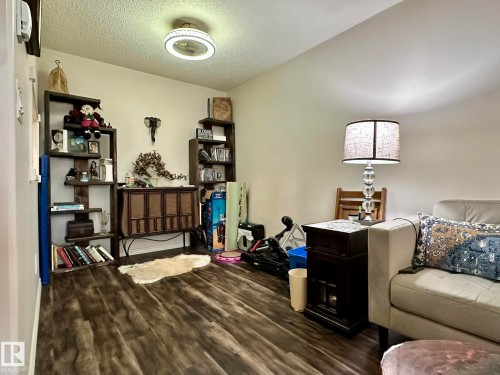 Spacious living area featuring wood-finish flooring, light-colored walls, and a contemporary ceiling light fixture - 211 9619 174 Street, Edmonton, AB - Indoor