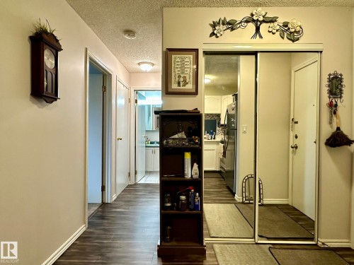 Hallway with wood-finish flooring extending into the kitchen, featuring a mirrored closet with sliding doors and a white entry door - 211 9619 174 Street, Edmonton, AB - Indoor Photo Showing Other Room