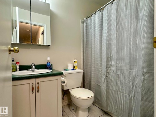 Bathroom featuring a white toilet, light-colored vanity with green countertop, and a mirrored medicine cabinet - 211 9619 174 Street, Edmonton, AB - Indoor Photo Showing Bathroom