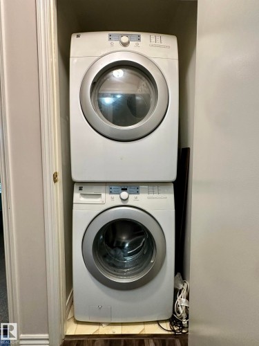 Dedicated laundry closet featuring a stacked white washer and dryer unit with front-loading doors - 211 9619 174 Street, Edmonton, AB - Indoor Photo Showing Laundry Room