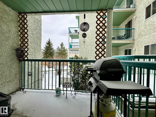 Private balcony featuring a textured exterior wall, green metal railing, and a slatted privacy screen - 211 9619 174 Street, Edmonton, AB - Outdoor With Balcony With Exterior