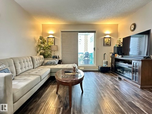 Living area featuring wood-finish flooring, a sliding glass door, and a built-in wall sconce - 211 9619 174 Street, Edmonton, AB - Indoor Photo Showing Living Room