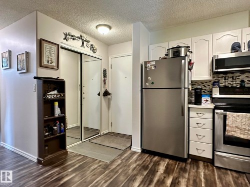 Kitchen area featuring wood-finish flooring, white cabinetry, stainless steel refrigerator, and range - 211 9619 174 Street, Edmonton, AB - Indoor Photo Showing Kitchen With Stainless Steel Kitchen
