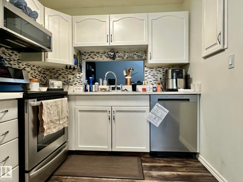 Kitchen featuring white shaker-style cabinetry, a mosaic tile backsplash, and wood-finish flooring - 211 9619 174 Street, Edmonton, AB - Indoor Photo Showing Kitchen