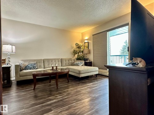 Living area featuring wood-finish flooring, light neutral wall tones, and a sliding glass door to a balcony - 211 9619 174 Street, Edmonton, AB - Indoor Photo Showing Living Room